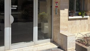 Una entrada de edificio con puerta de vidrio, señal de alarma contra incendios y ventana con plantas en macetas.