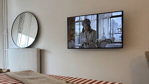 Un dormitorio con una colcha a rayas, un espejo redondo y un televisor mostrando una escena.