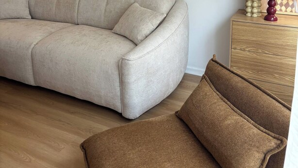 Un sofá beige con un cojín, una mesita de madera con objetos decorativos y un cuadro en la pared.