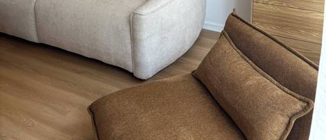 A beige sofa with a cushion, a wooden side table with decorative items, and a painting on the wall.