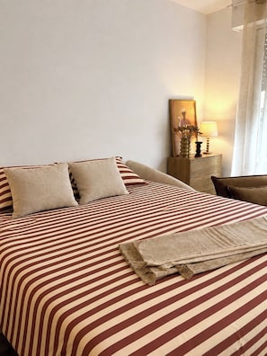 Et hotelværelse med en stor seng, to puder, et sengebord med en lampe og et billede i ramme på væggen.