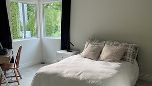 Ett sovrum med en stor säng, ett skrivbord och en stol. Det finns två fönster med gardiner och en taklampa.