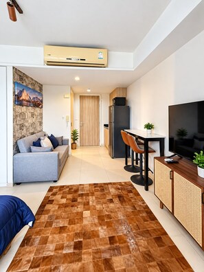 A modern living room with a sofa, a dining table with chairs, a TV, and a kitchen area with a refrigerator. - 10 Mins walk to Walking Street Apartment in Pattaya Jomtien (ตำบล หนองปรือ)