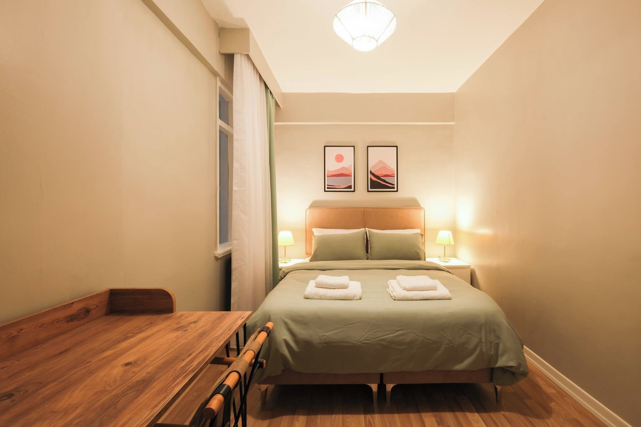 A hotel room with a wooden bed, two bedside lamps, a wooden table, and a window with curtains.