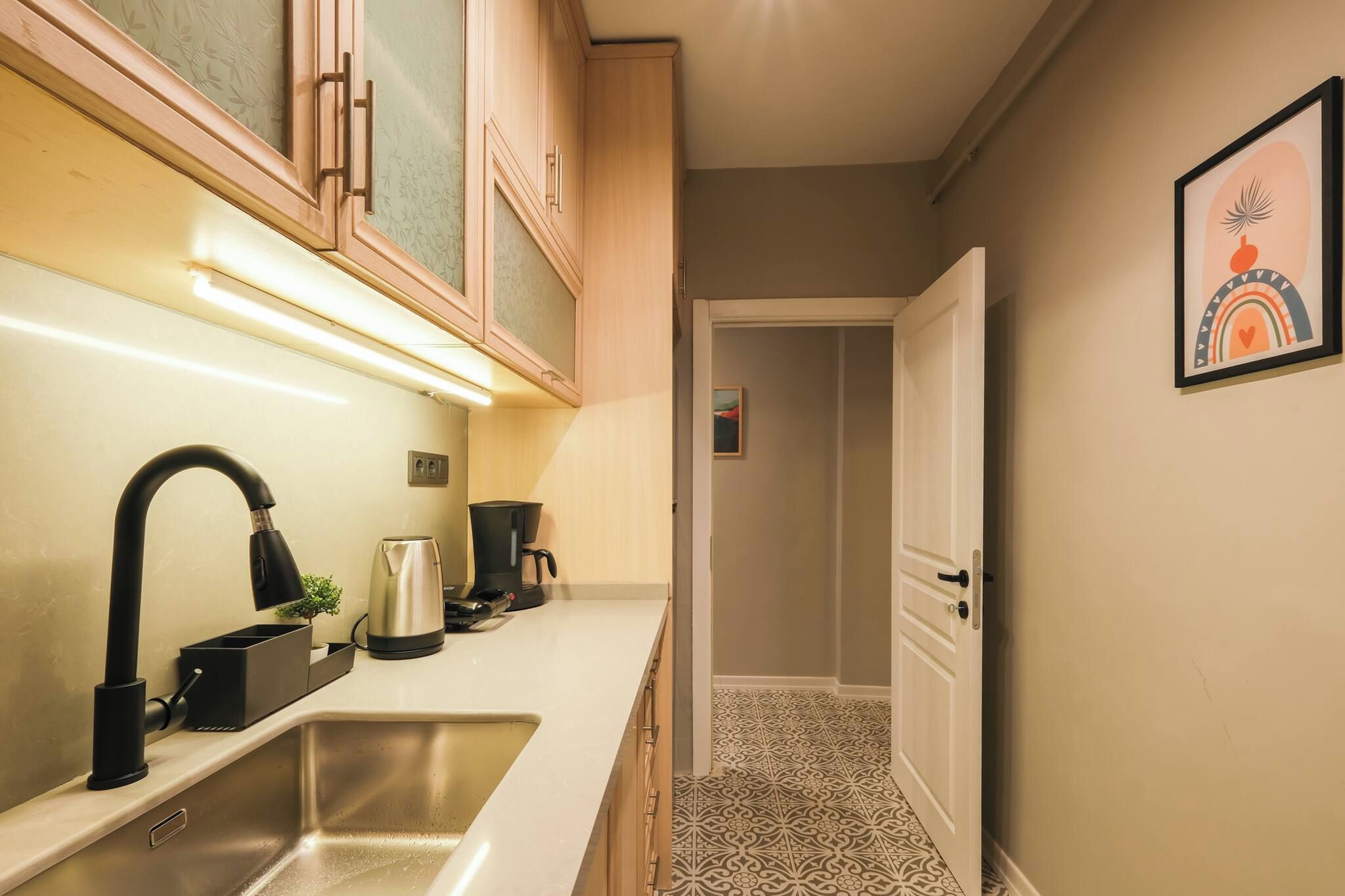 A kitchen with a sink, a coffee maker, and a kettle. There is a door leading to another room.