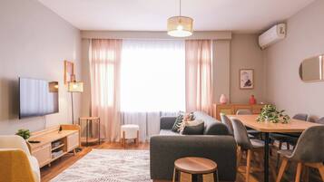 A modern living room with a flat-screen TV, sofa, dining table, and chairs.