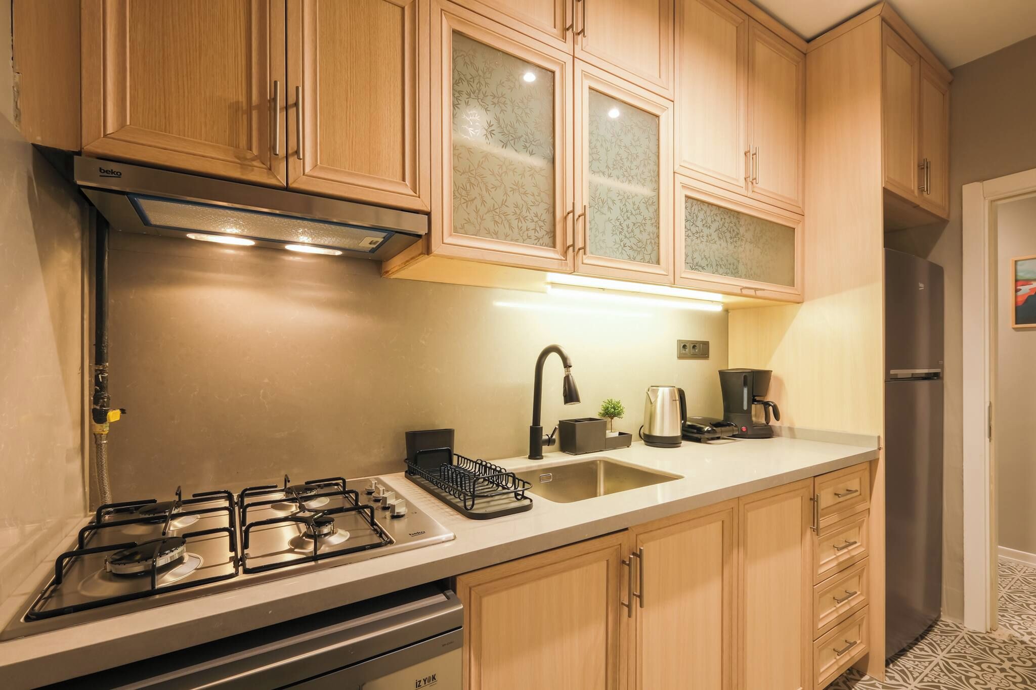 A kitchen with wooden cabinets, a gas stove, a sink, and a refrigerator.