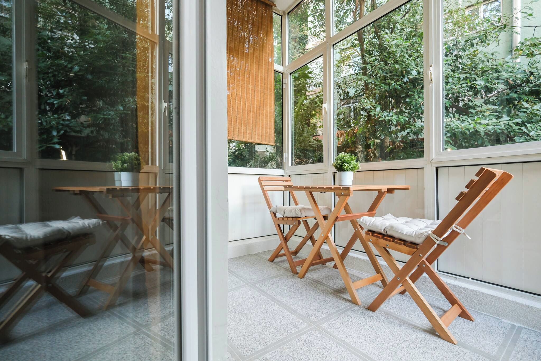 A room with a glass partition, a wooden table with chairs, and a view of greenery outside.