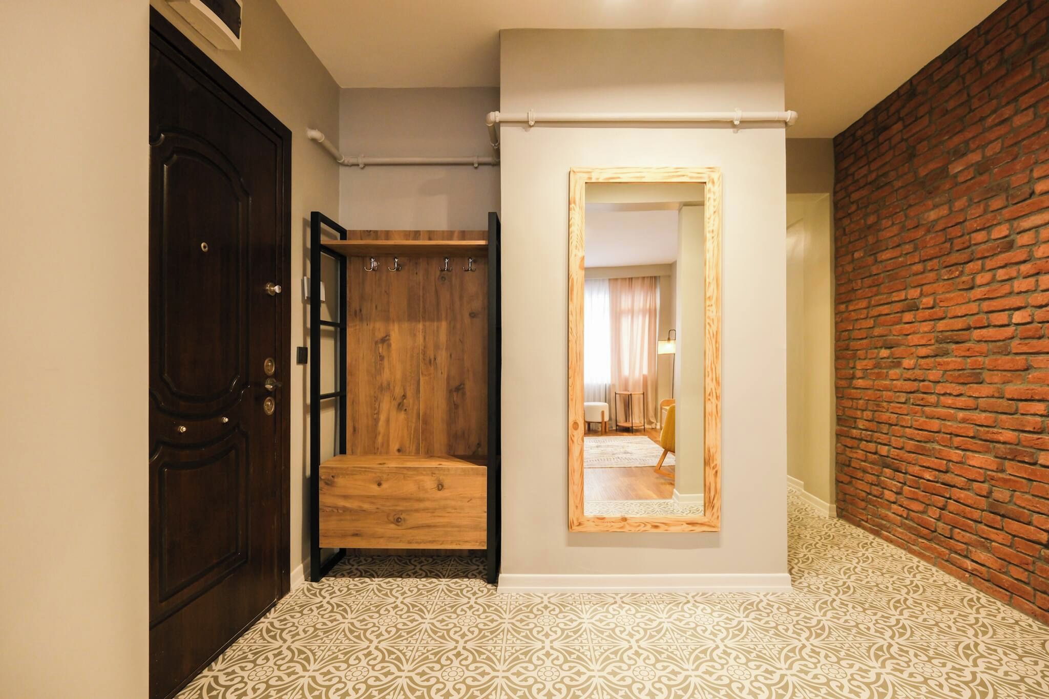 A hallway with a patterned floor, a wooden door, a mirror, and a brick wall.