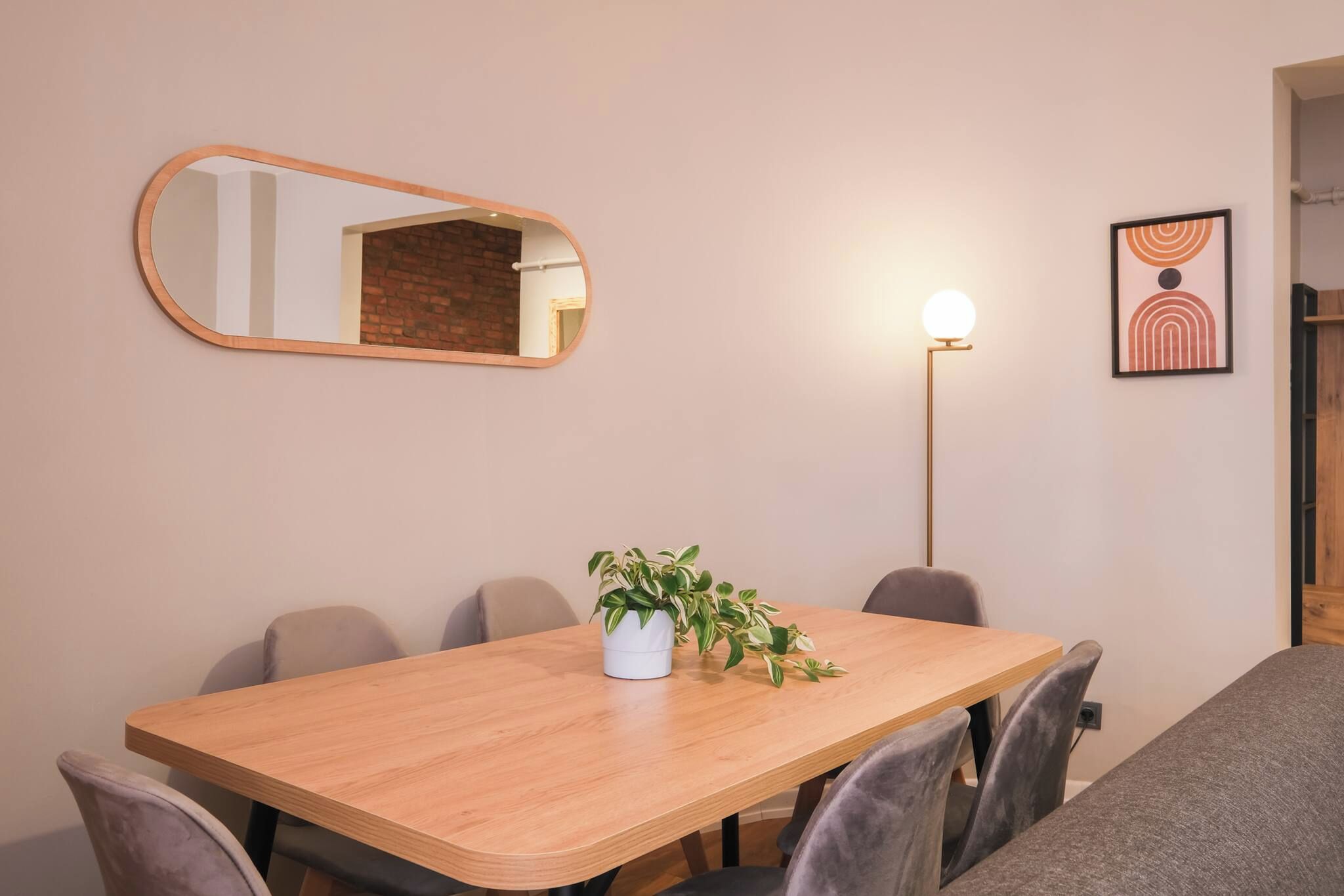 A conference room with a wooden table, chairs, a potted plant, a mirror, a floor lamp, and a framed picture on the wall.