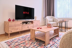 A living room with a wooden TV stand, a flat-screen TV, a potted plant, a small table, and a patterned rug. - Historical Building at the Iconic Tram Street, 3BR (Kadıköy)