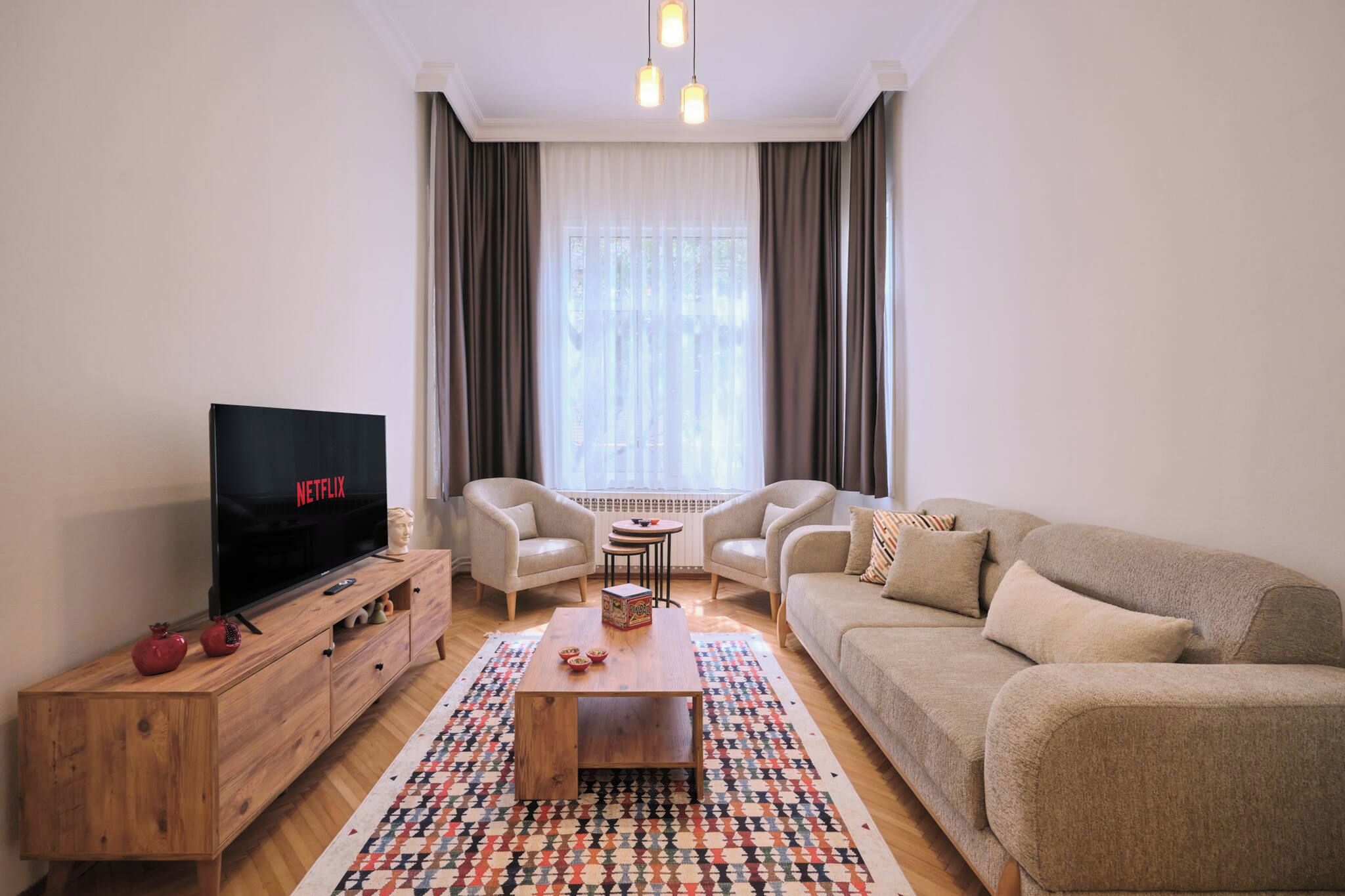 A living room with a TV, sofa, chairs, a coffee table, and a patterned rug.