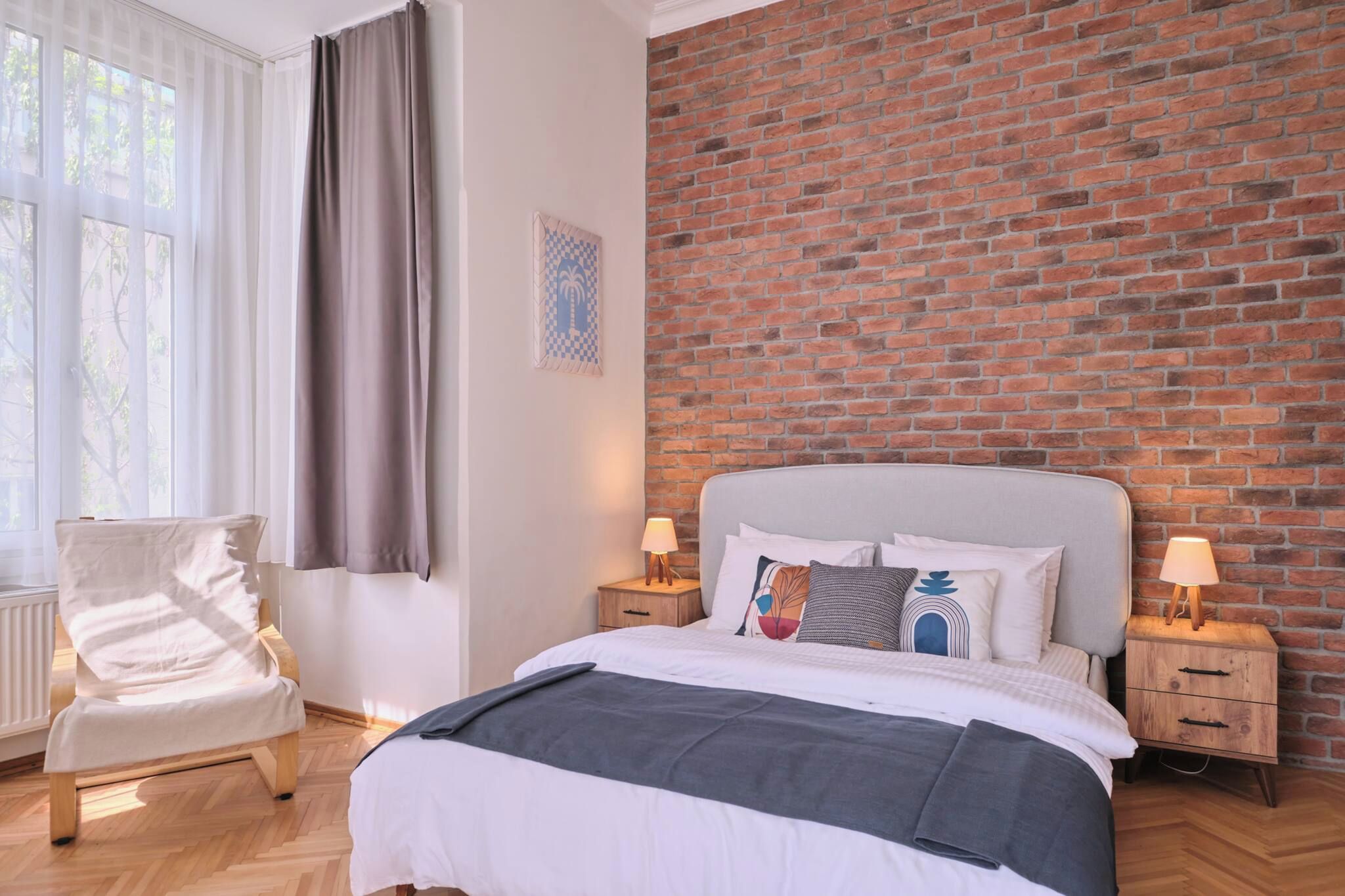 Ein Schlafzimmer mit Backsteinwand, einem Bett mit weißer Bettwäsche, einem Sessel und zwei Nachttischen mit Lampen.