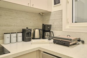 Eine Küchenzeile mit Kaffeemaschine, Zucker- und Teeausgabesystem, Wasserkocher und einem tragbaren Grill.
