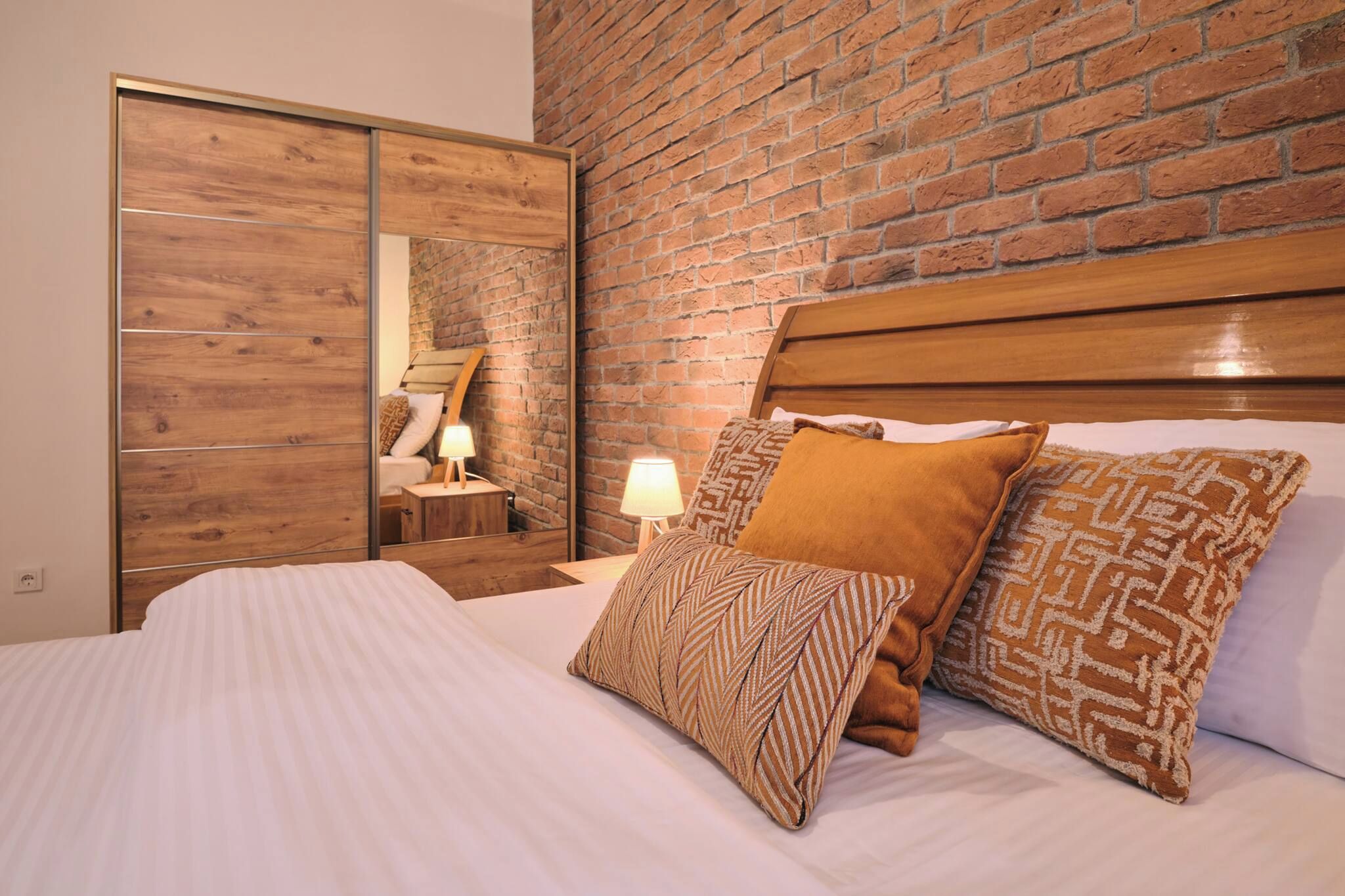 A hotel room with a brick wall, a wooden headboard, and a bed with patterned pillows.