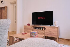 A living room with a wooden coffee table, a television displaying the Netflix logo, a small cabinet with decorative items, and a statue on a stand. - Historical Building at the Iconic Tram Street, 3BR (Kadıköy)