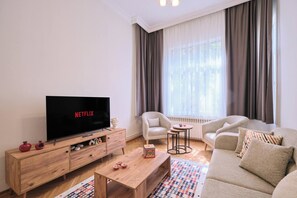 Ein Wohnzimmer mit Fernseher, einer Couch, einem Sessel, einem Couchtisch und einer Heizung.
