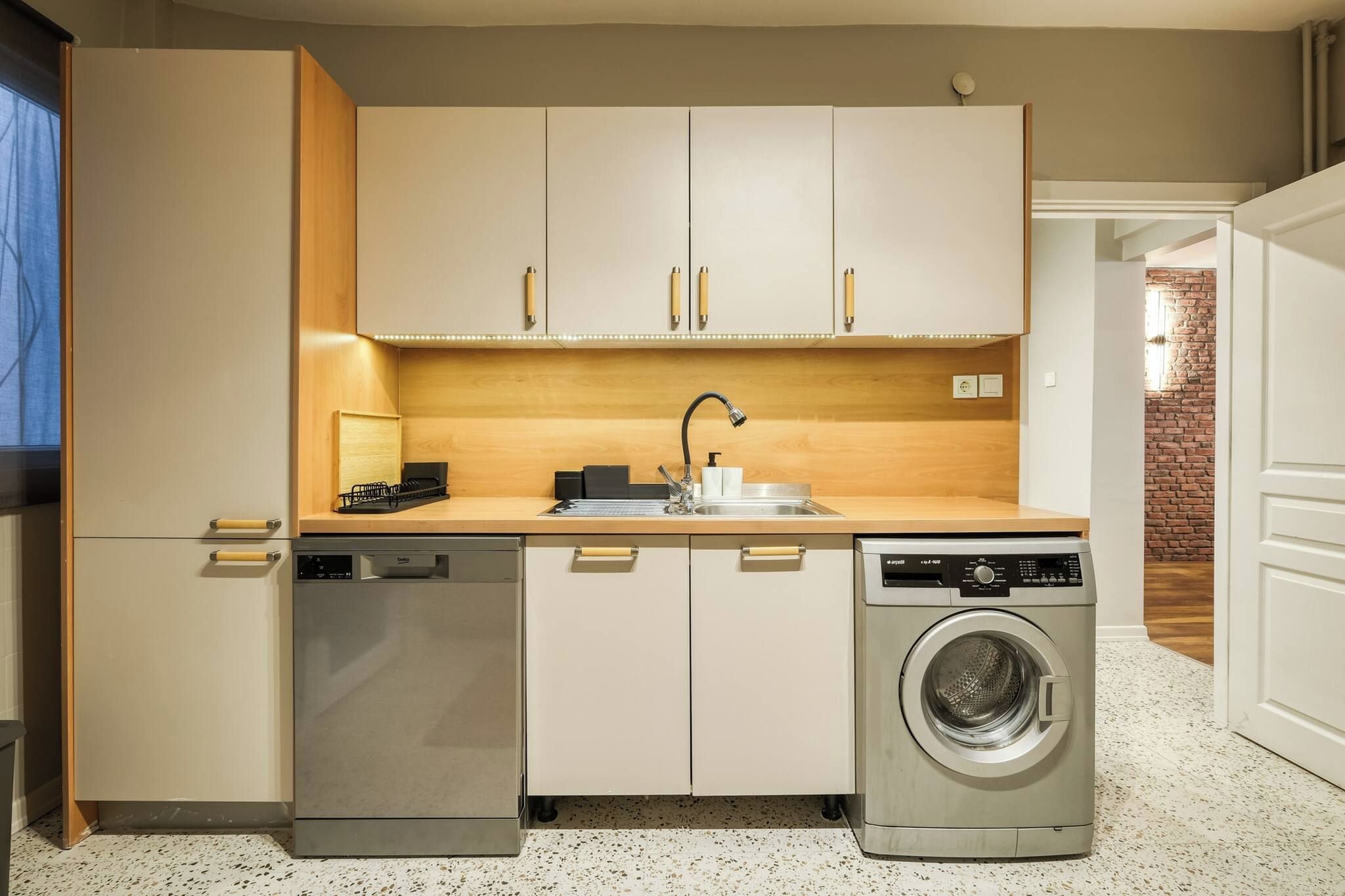 A compact kitchen with a dishwasher, washing machine, and a sink with a modern faucet.