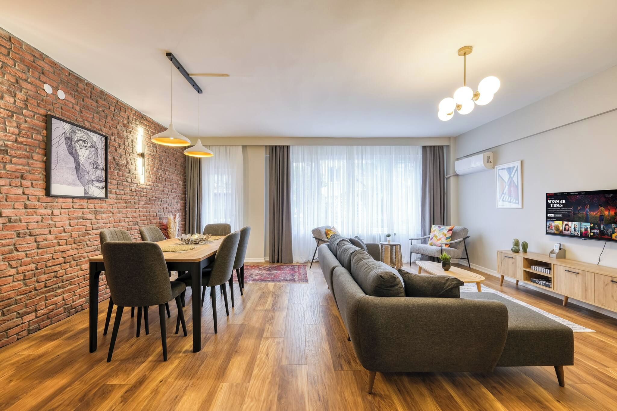 Ein modernes Wohnzimmer mit Essbereich, einer Sofagarnitur, einem Fernseher und einer Ziegelwand.