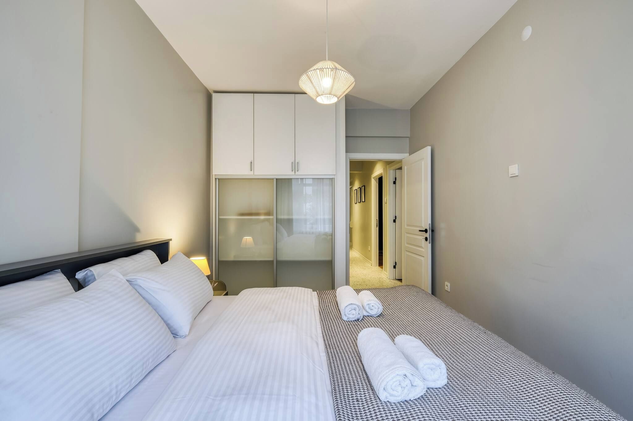 Ett hotellrum med en säng, en garderob, en hängande lampa och en dörr som leder till ett annat rum.