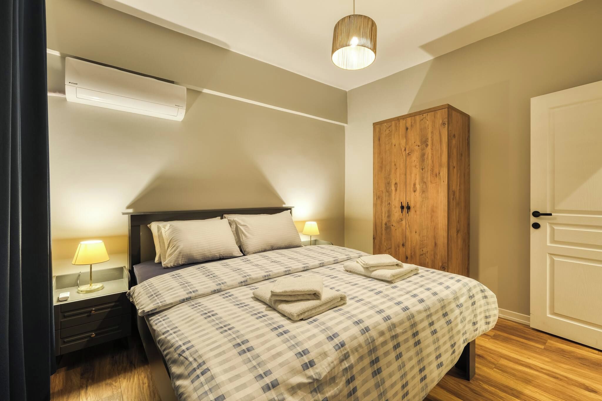 A bedroom with a bed, nightstands, a lamp, a wardrobe, and an air conditioning unit.