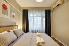 A hotel room with a bed, two pillows, a headboard, a window with curtains, and an air conditioning unit. - Prestige, Spacious, 3BR (Kadıköy)