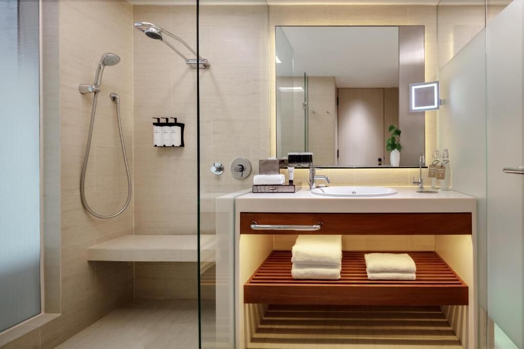 Ein modernes Badezimmer mit einer gläsernen Dusche, einem Waschtisch inklusive Spiegel und einem Holzregal.