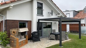 A house with a covered patio area, a wicker sofa, a grill, and a dining table. - Holiday home with 1 bedroom (Krakow am See)