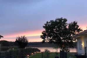 A serene lakeside view at dusk with a house, a tree, and a fence. - Holiday home with 1 bedroom (Krakow am See)