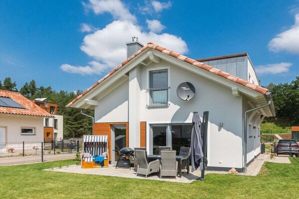 Ein modernes, zweistöckiges Haus mit einer Terrasse, die Gartenmöbel und einen Grill hat.