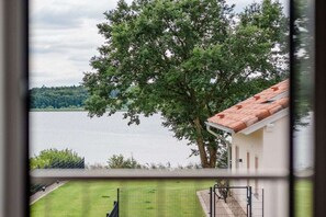 A view of a lake with a tree in the foreground and a building with a red roof in the background. - Holiday home with 1 bedroom (Krakow am See)