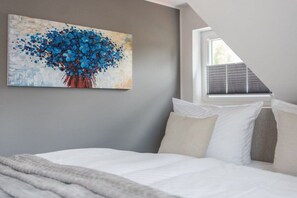 A bedroom with a bed, pillows, a painting, and a window with blinds. - Holiday home with 1 bedroom (Krakow am See)
