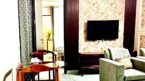 Uma sala de estar com sofá, televisão presa na parede, uma cadeira de madeira e papel de parede estampado.