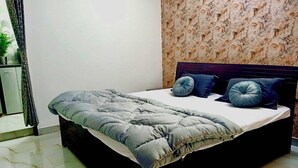 Cama com cabeceira escura, colcha cinza e duas almofadas azuis.