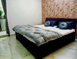 Una cama con cabecera oscura, colcha gris y dos almohadas azules.