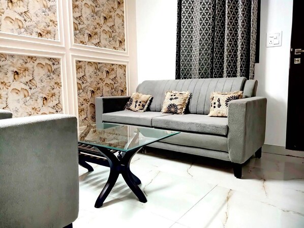 Una sala de estar con un sofá gris, cojines estampados, una mesa de centro de vidrio y un sillón.