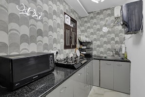 A kitchen with a black microwave, a gas stove, and a sink. - Welcome to Lutyens Imperial, a spacious and thoughtfully designed apartment. (New Delhi)