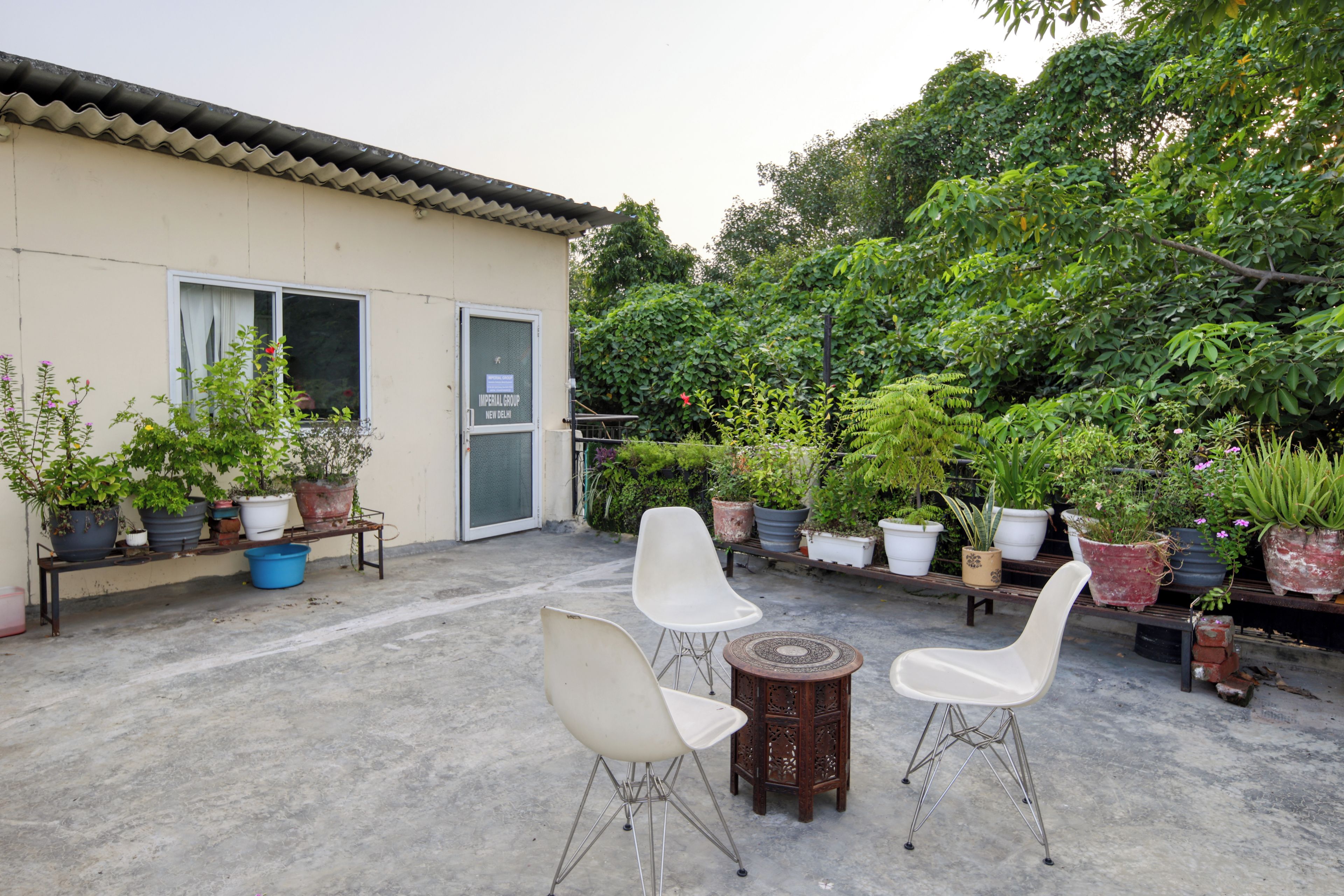 An outdoor patio with two white chairs, a small round table, and various potted plants.