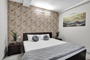 A bedroom with a floral wallpaper, a bed with grey bedding, a nightstand with a plant, and a painting on the wall.