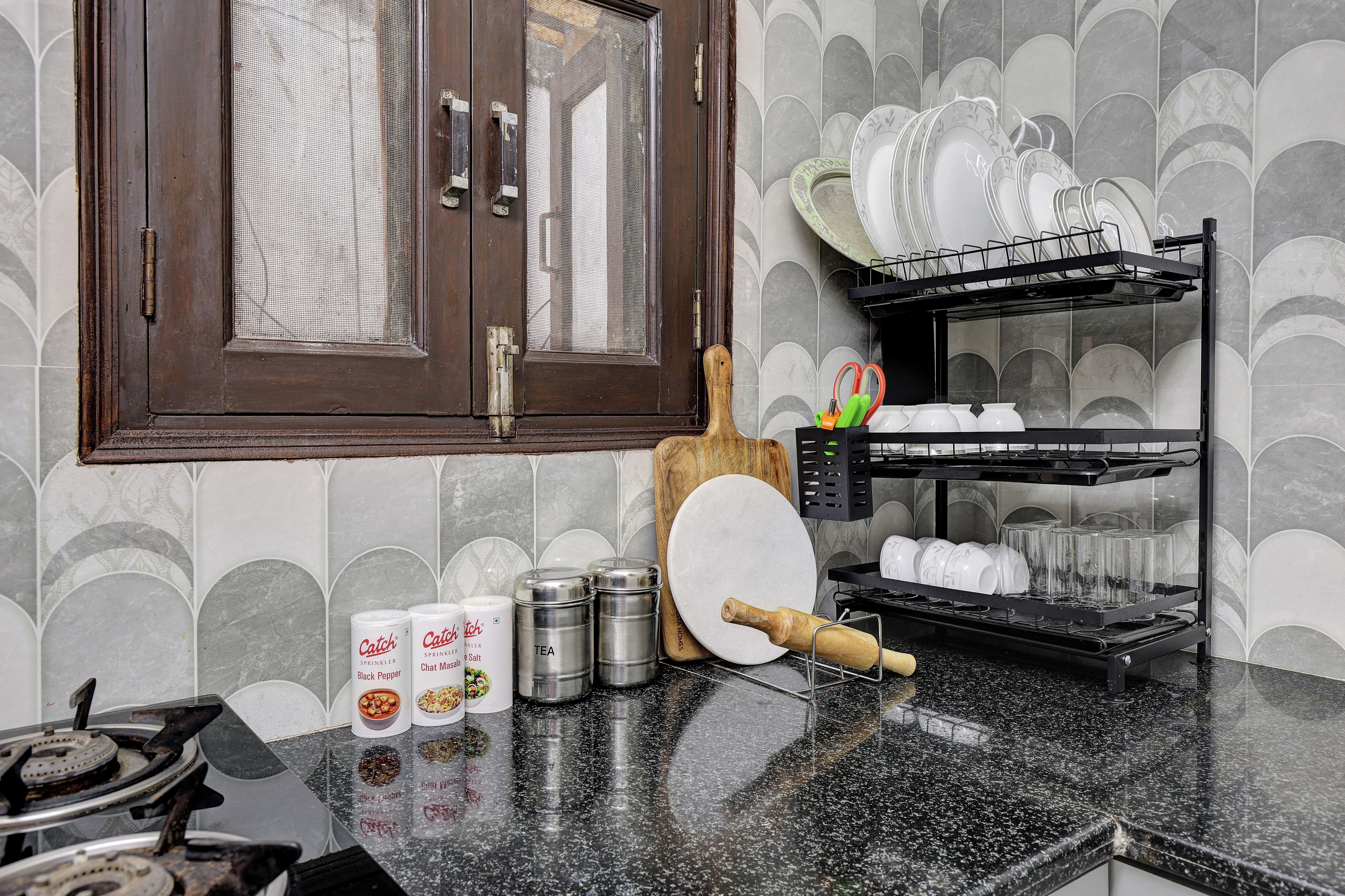 A kitchen with a wooden door, a spice rack, a dish rack, and a countertop with various kitchen items.