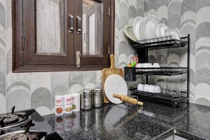 Una cocina con puerta de madera, un estante para especias, un escurreplatos y una encimera con diversos utensilios de cocina.