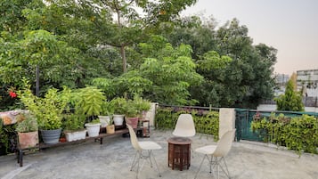 An outdoor seating area with a concrete floor, surrounded by potted plants and trees.