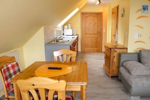 A compact living space with a dining table, chairs, a sofa, a kitchenette, and a wooden door. - Behind the dunes - W87 (Prerow)