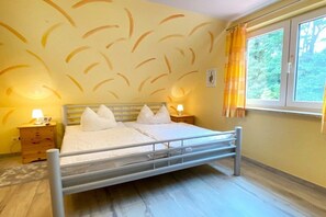 A single-bed room with a metal frame, two bedside tables with lamps, a window with curtains, and a wall with a leaf pattern. - Behind the dunes - W87 (Prerow)