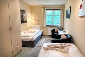 Un dormitorio con una cama, un escritorio y una silla. Se ve una ventana con cortinas.