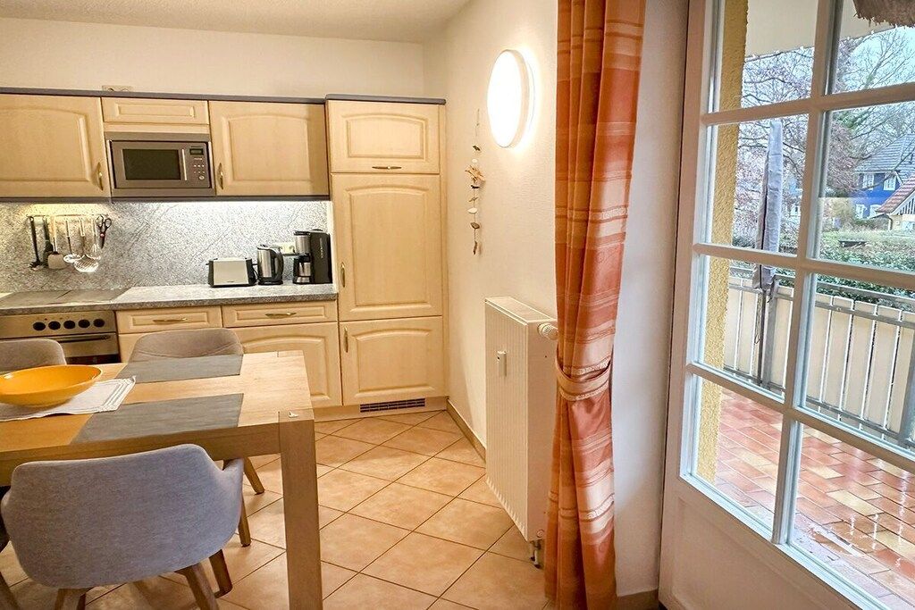 Eine kompakte Küche mit Esstisch, Stühlen und einem Fenster mit Vorhängen.