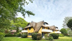 Ein gelbes Gebäude mit einem einzigartigen architektonischen Design, das mehrere Balkone und einen gepflegten Garten aufweist.