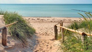 Ein Sandstrand mit einem hölzernen Pfad, der zum Wasser führt, umgeben von Gras.