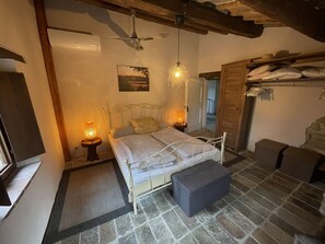 Ein Schlafzimmer mit einem Bett, zwei Nachttischlampen, einem Deckenventilator, Steinböden und einer Holztür.