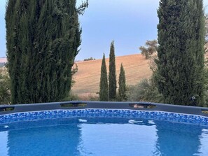 Ein Pool mit Fliesenrand, umgeben von hochwachsenden immergrünen Bäumen, mit Blick auf eine hügelige Landschaft im Hintergrund.